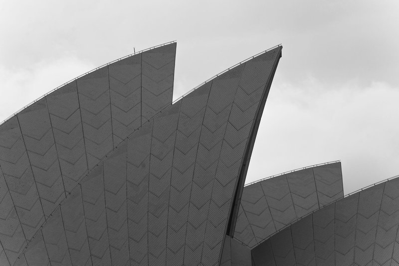 Low angle of black and white shell shaped geometric roof of Sydney Opera House against cloudy sky