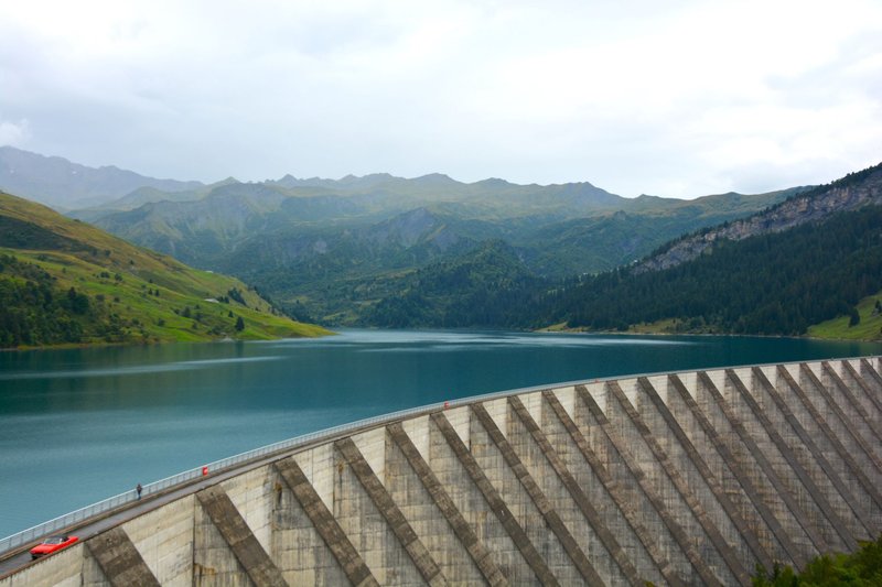 A scenic mountain landscape featuring a large dam and serene lake reflection.