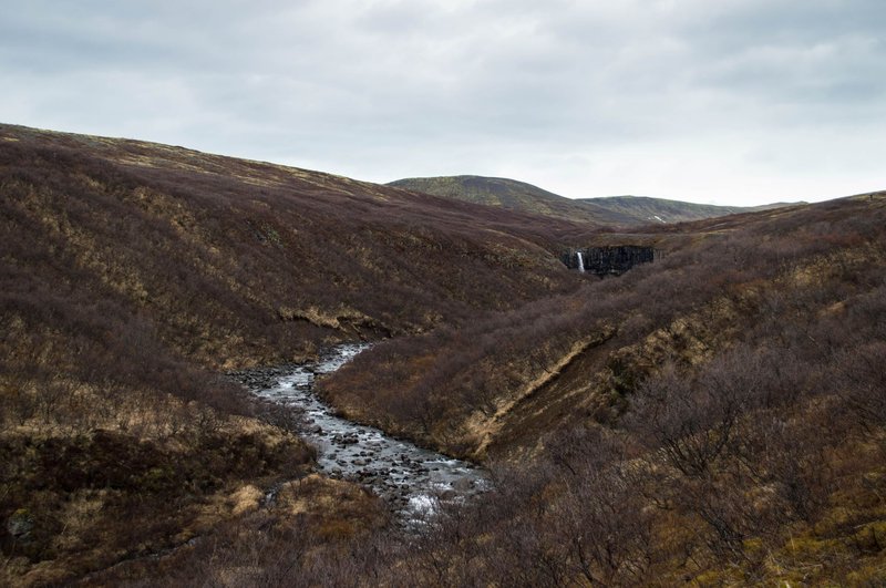 Explore the serene beauty of Iceland's rugged landscape featuring a cascading waterfall and tranquil river.
