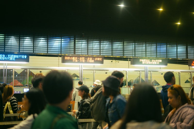 Crowded airport check-in area with people queueing and visible flight information signs.