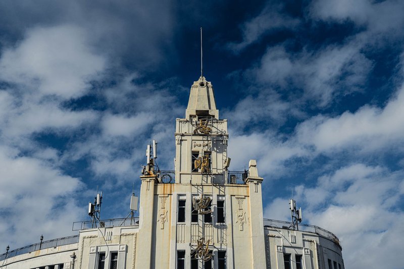 Exterior of building with small windows and tower located against blue sky with clouds on street in city with bright sunlight