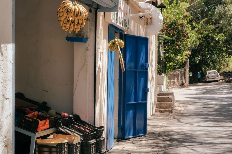A vibrant fruit market scene in Beirut with hanging bananas and blue entrance.