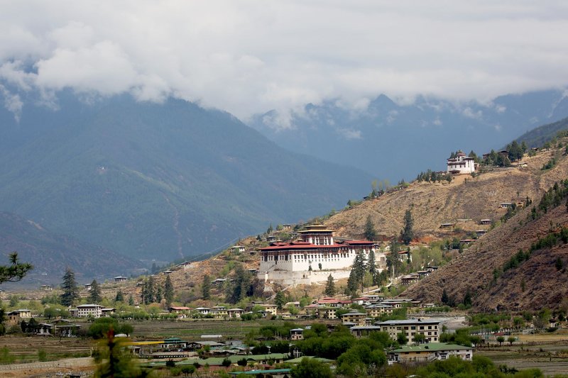 Scenic view of Paro Valley with Rinpung Dzong, surrounded by mountains and clouds in Bhutan.