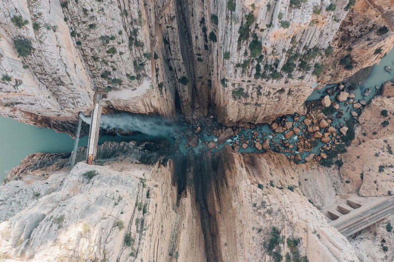 A breathtaking vertical shot of a canyon with a river flowing through, seen from above.