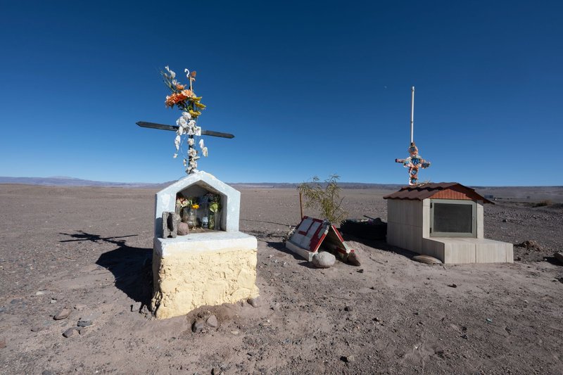 A desert roadside memorial with crosses in Antofagasta, Chile under a clear blue sky.