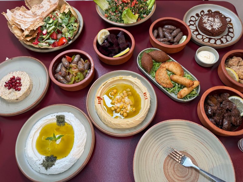 Assorted Middle Eastern dishes with hummus, tabbouleh, and more on a burgundy table.