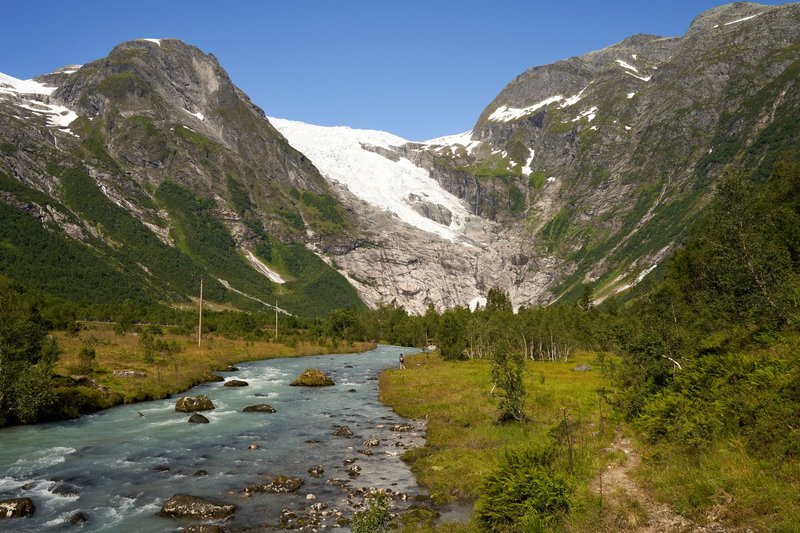 Breathtaking view of mountains with melting glacier and clear river under a blue sky.