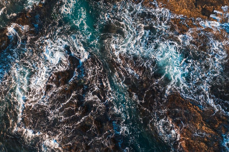Aerial view of turbulent ocean waves crashing against rugged rocks, showcasing nature's raw power.