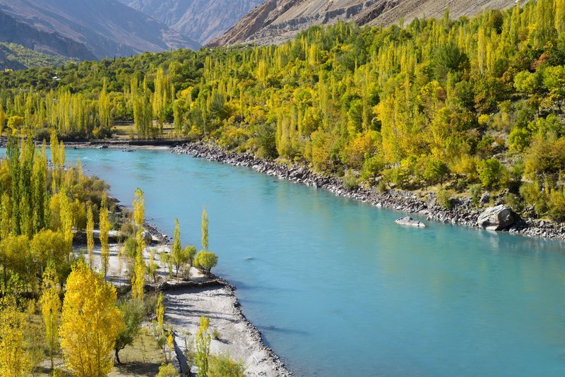 Vibrant autumn colors along a picturesque river in a majestic valley setting.