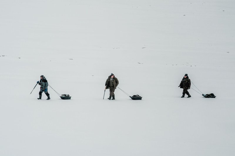 Three adults with sleds trekking across a snowy landscape, showcasing winter adventure and exploration.