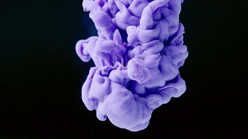 Vivid purple ink swirling in water creating abstract art against a dark background.