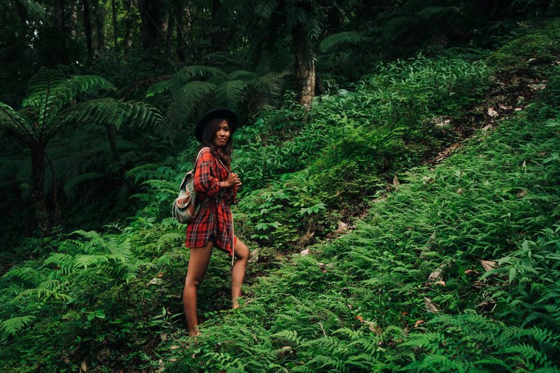Woman in plaid shirt hikes through a lush jungle, surrounded by vibrant green ferns, capturing outdoor adventure.
