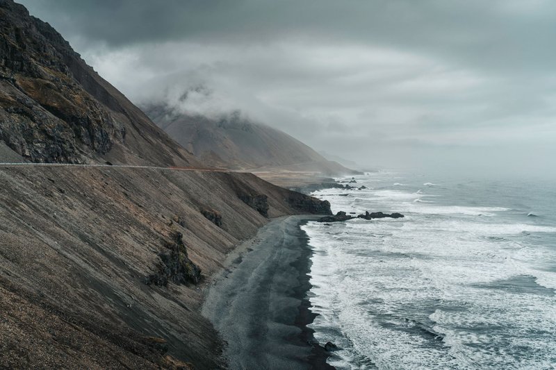 A breathtaking view of Iceland's rugged coastline with dark sand beaches and turbulent waves under a moody sky.