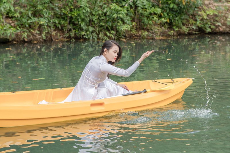 A woman in white enjoys a serene canoe ride on a calm river, surrounded by nature.