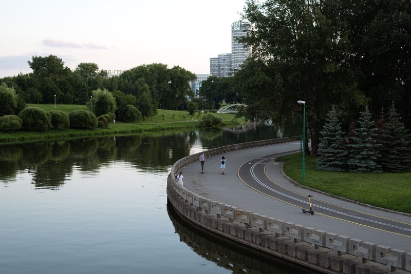 A serene view of people walking along a riverside promenade in an urban park during summer.