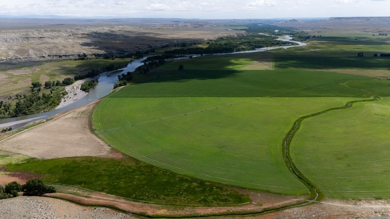 Panoramic aerial shot of lush green farmland with irrigation circle and nearby winding river.