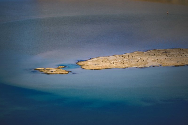 A serene aerial view of a small deserted islet in calm blue waters.