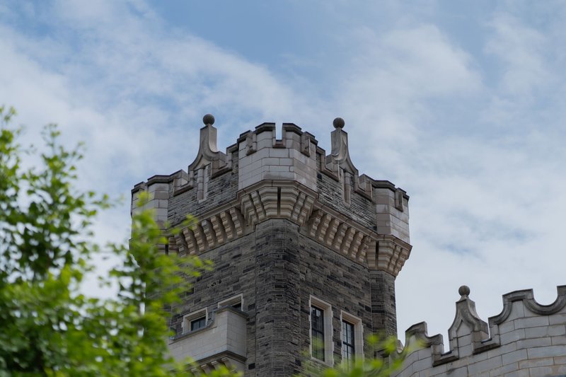 A majestic stone castle tower reaching towards a blue sky, surrounded by greenery.