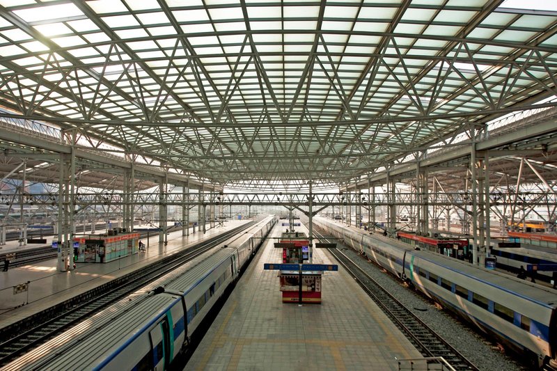 Spacious railway station with multiple platforms and trains under a steel glass roof.
