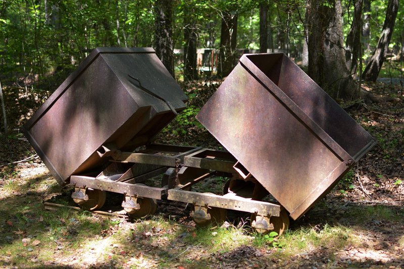 A vintage rusty mining cart sits in a sunlit forest, symbolizing industrial legacy.