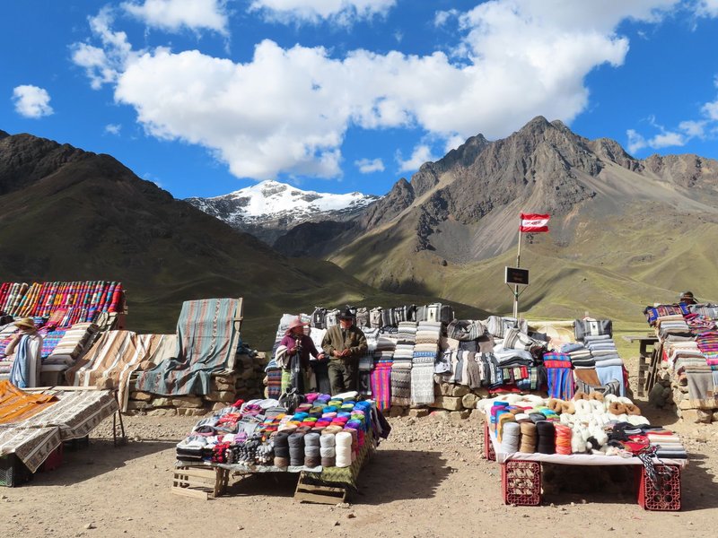Vibrant market stall showcasing textiles amidst the stunning Peruvian Andes backdrop.