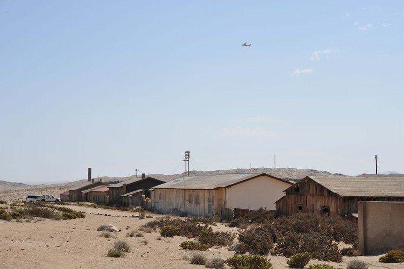 Barren landscape with abandoned buildings in Kolmanskop, Namibia under a clear blue sky.
