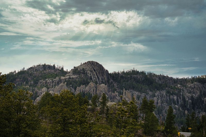 Dramatic landscape of the Black Hills with rocky mountains and lush forests under cloudy skies.