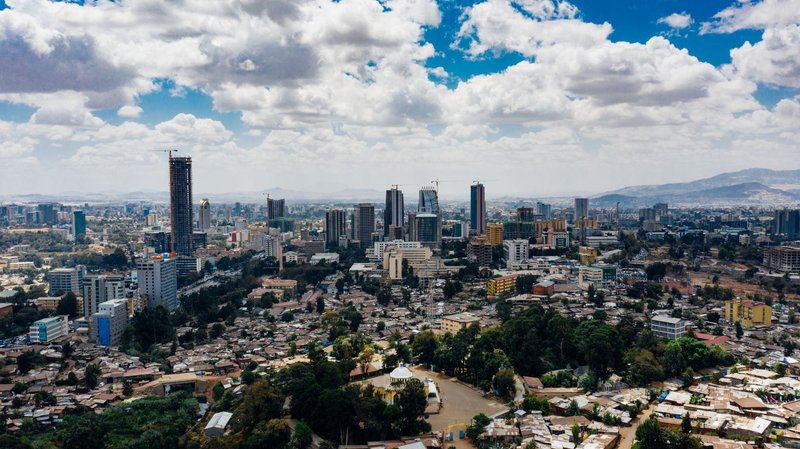From above of scenery view of contemporary city with high multistage buildings and trees with mountains far away under sky with clouds in daylight