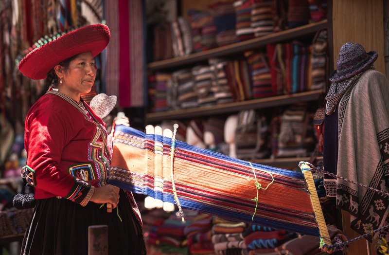 Inca woman weaving vibrant textiles at a colorful market in Cusco, Peru.