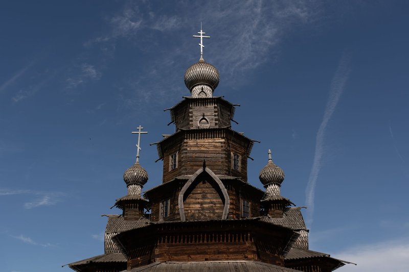 Capture of an ancient wooden church with onion-shaped domes against a clear blue sky.