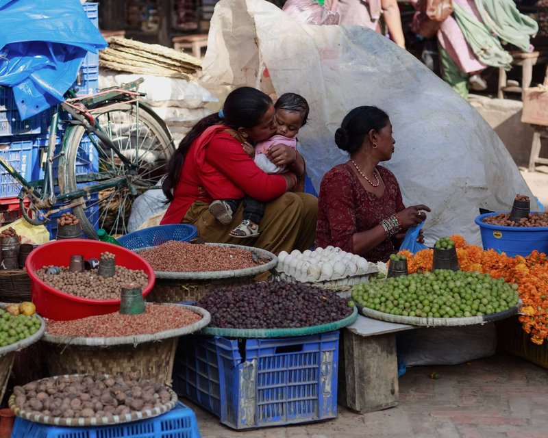 A touching family moment at a lively outdoor market with diverse fresh produce on display.