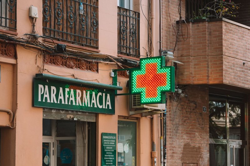 A street view of a parafarmacia with a glowing neon cross, showcasing urban pharmacy architecture.
