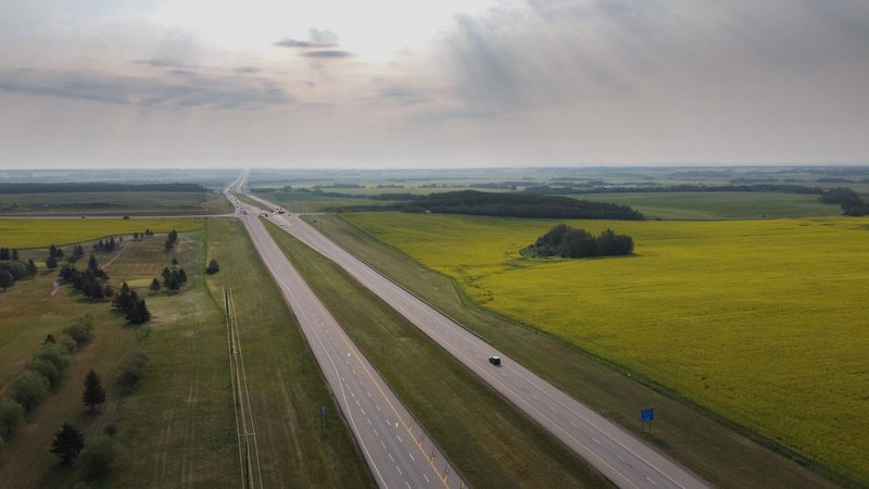 Stunning aerial view of Sylvan Lake highway with expansive fields under a summer sky.