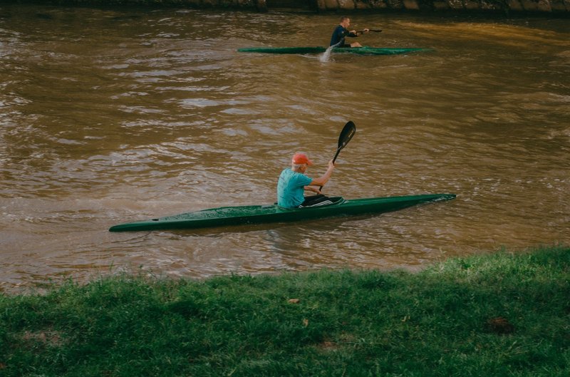 Two adults kayaking on a flowing river, enjoying outdoor leisure activities in summer.