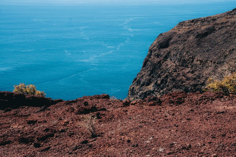 Red volcanic cliffs meeting the deep blue ocean in Alajeró, Canary Islands.