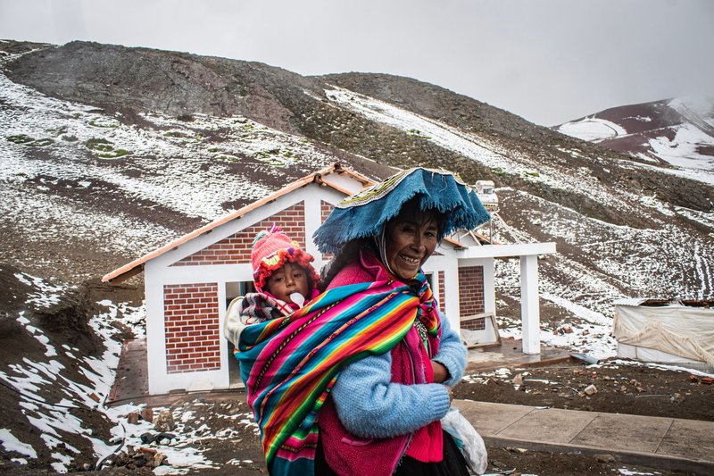Mother and child in colorful traditional attire in snowy Andean village setting.