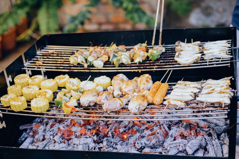 A variety of foods grilling over hot coals in an outdoor barbecue setup.