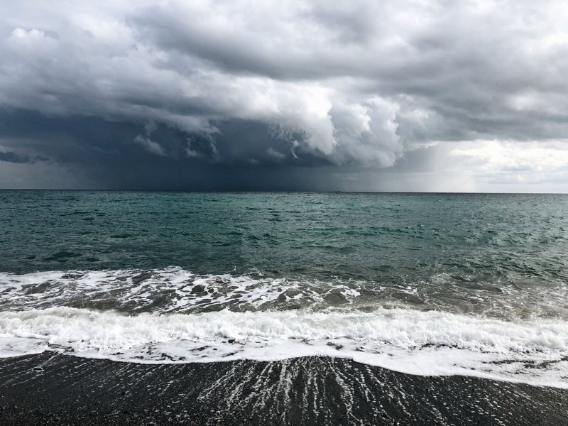 Dramatic thick clouds floating over rippling sea with foamy waves rolling on black sandy beach