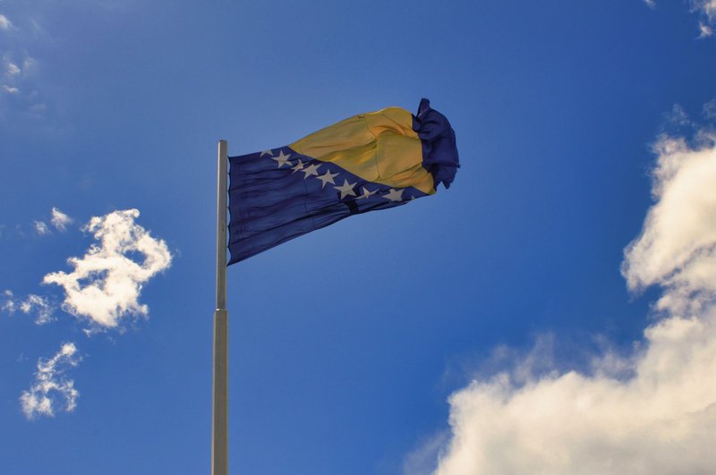 Bosnia and Herzegovina flag on a pole with a clear blue sky background in Mostar.