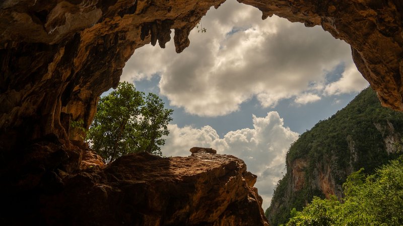 Scenic view from inside a cave in Cuba showing a cloudy sky and green landscape.