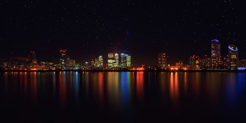 City skyline at night with shimmering water reflections and starry sky.