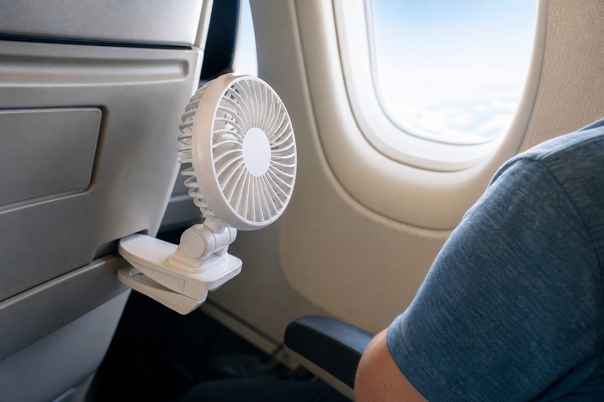Small white clip fan attached to the seatback in front of an airplane window seat