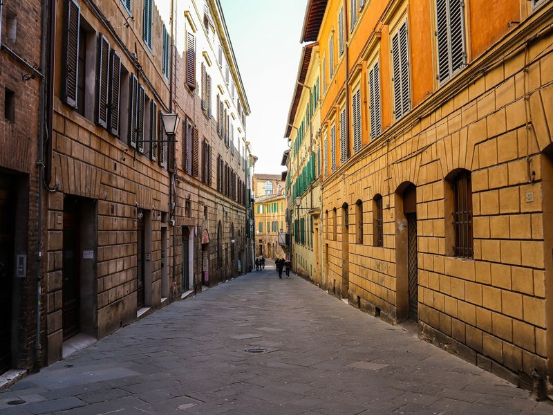 Quaint urban alley with vibrant building facades and shuttered windows, showcasing European architecture.