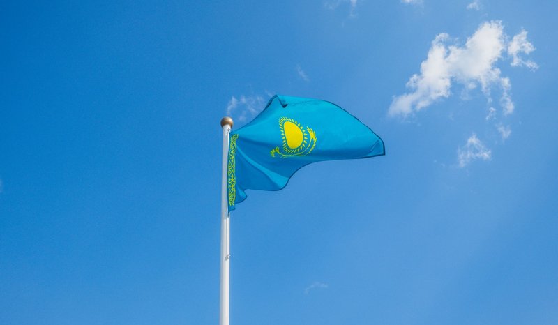 National flag of Kazakhstan waving on flagpole with clear blue sky background.