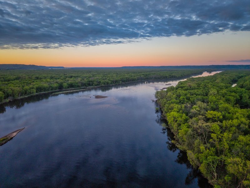 Stunning aerial view of the Mississippi River surrounded by lush forests under a vibrant sunset sky in Pepin, Wisconsin.