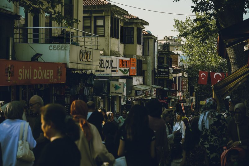 Crowded street market in Bursa, Türkiye with people shopping and Turkish flags displayed.