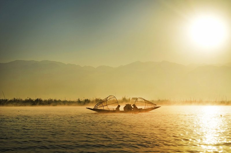 Silhouetted fishermen on tranquil Inle Lake at sunrise, Shan State, Myanmar.