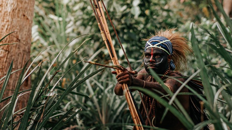 Tribal warrior with body paint and bow in Jayapura's lush jungle.