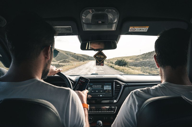 Two men driving through a scenic landscape, using a cellphone for navigation.
