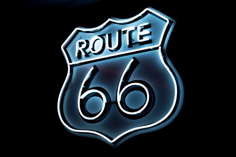 Bright neon Route 66 sign glowing on a black background, vintage style.